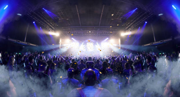 Concert crowd inside a venue, lens flare and smoke are visible